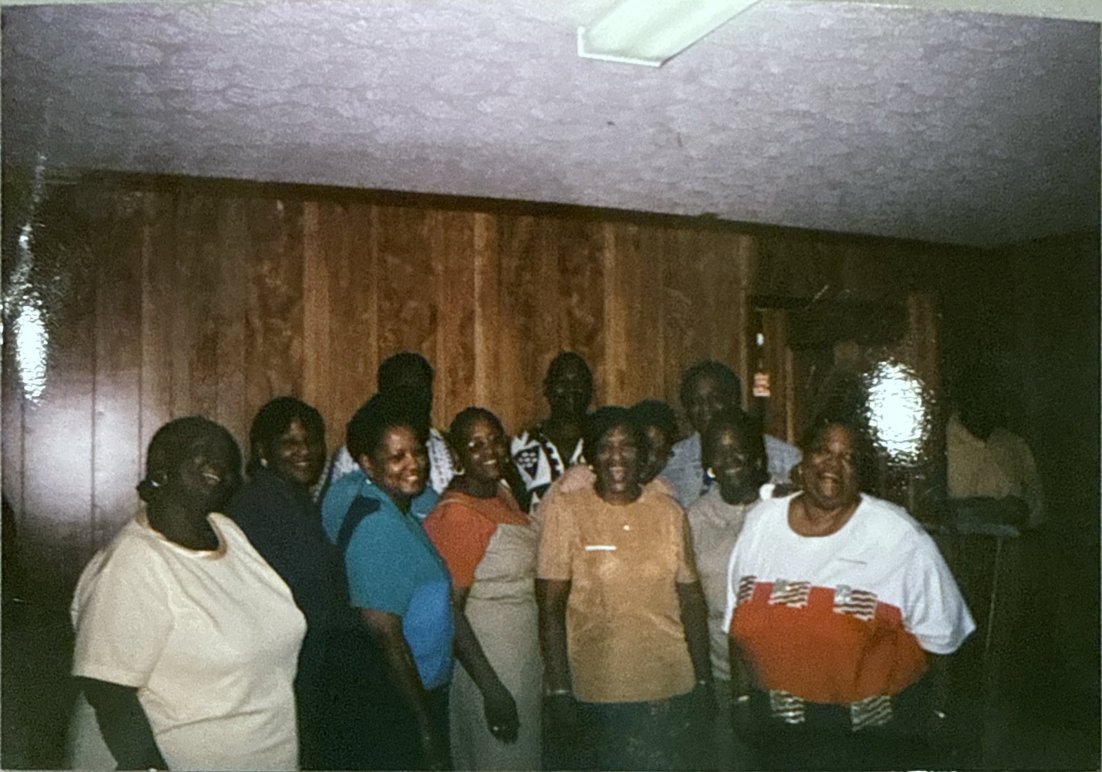 Older family photograph of about a dozen relatives smiling together in a wood-paneled room