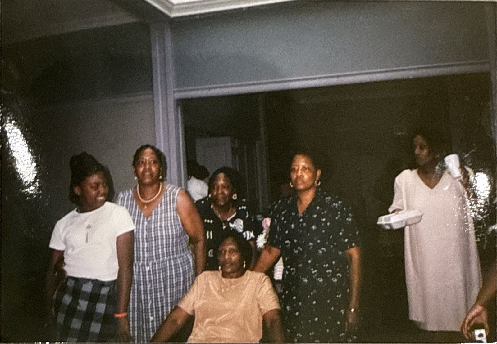 Older photograph of family members gathered around a seated elder at an indoor celebration