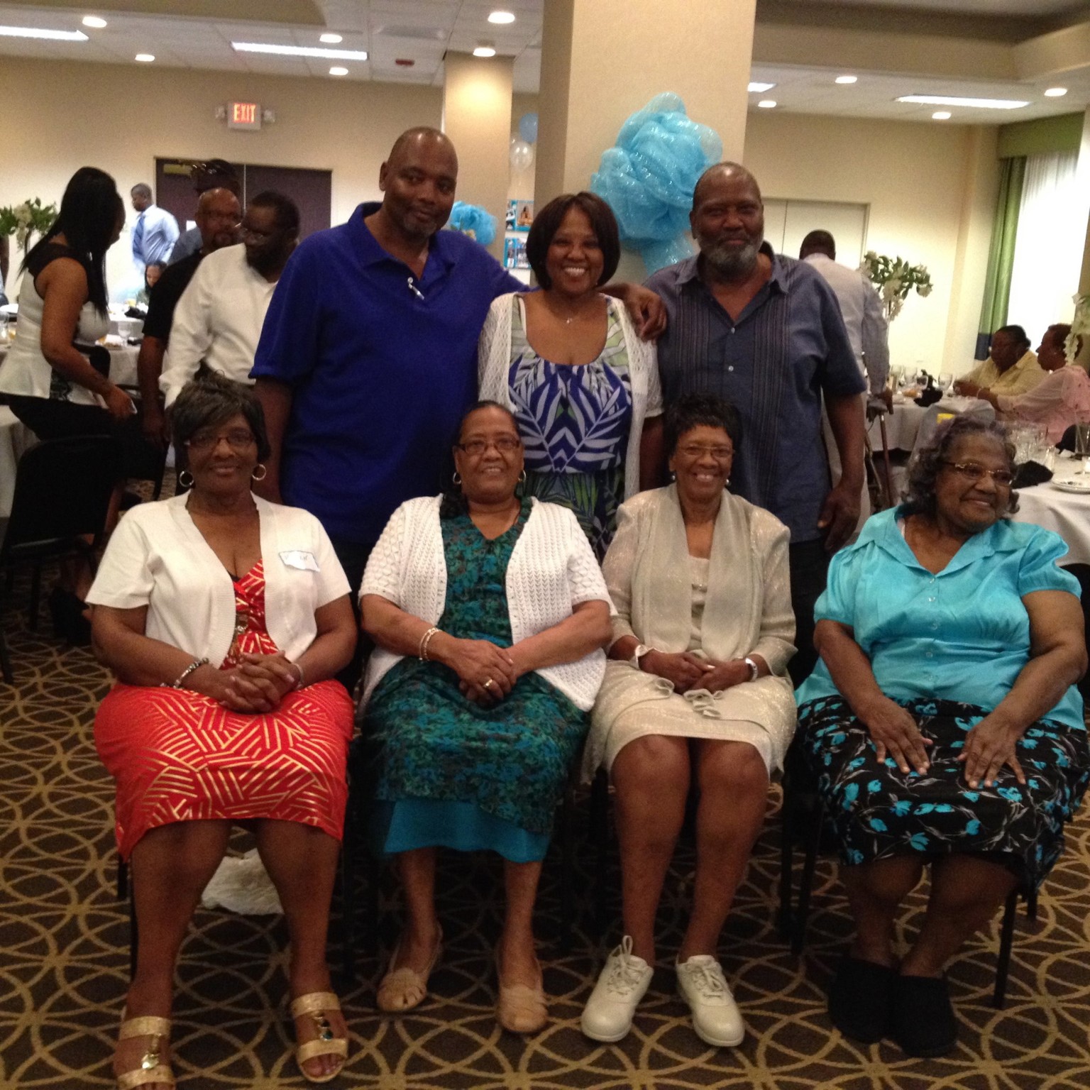 Family members gathered for a celebration, with four women seated in front